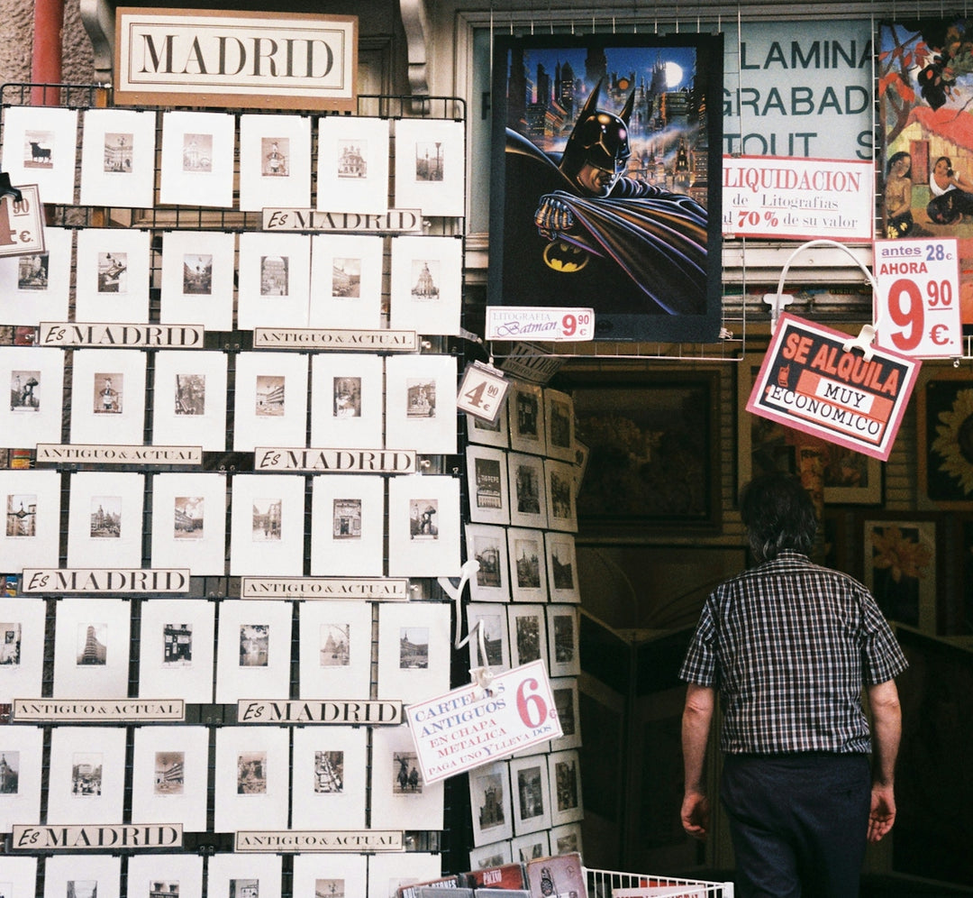 Man walks past a wall of small framed prints in madrid.