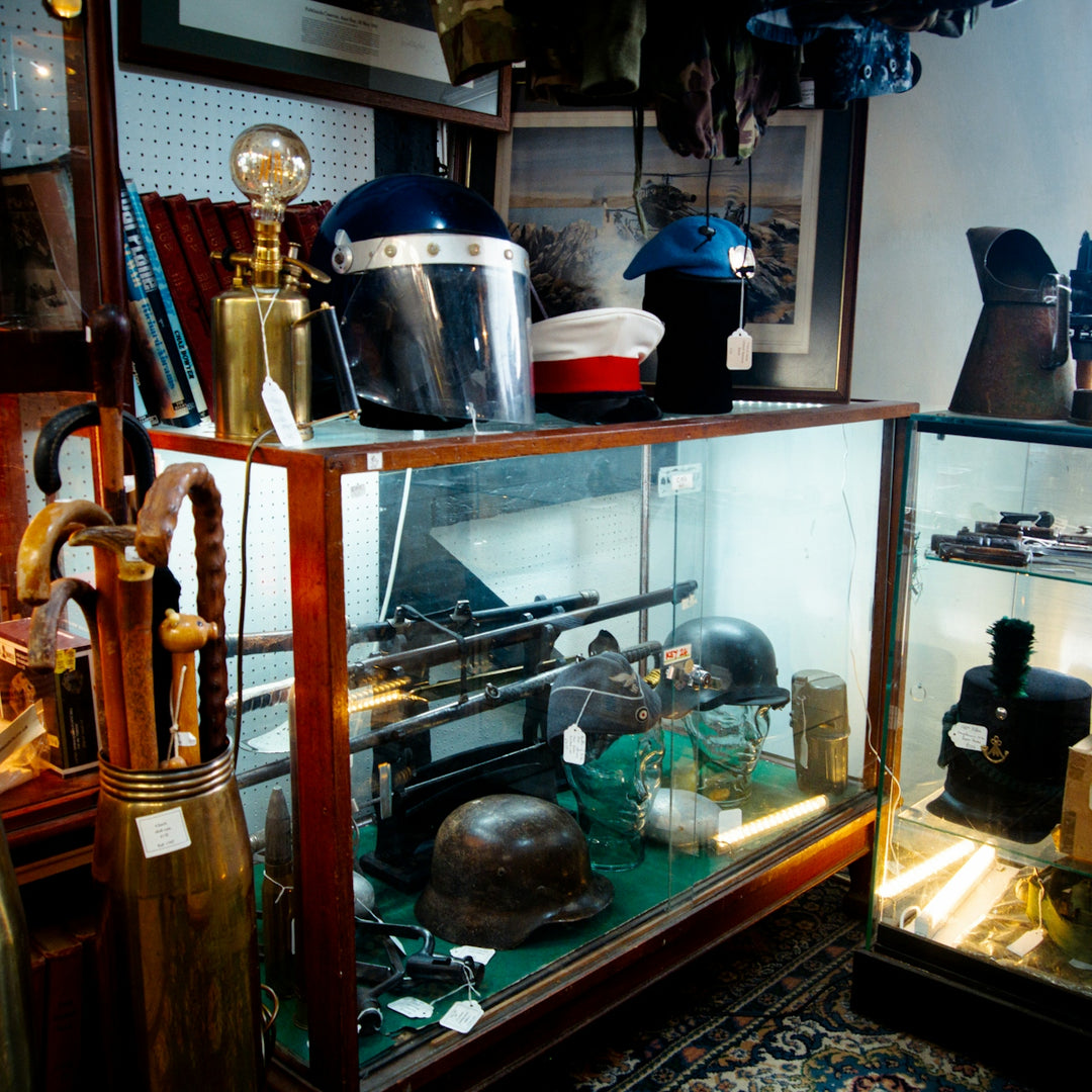 A glass display case containing vintage military helmets, hats, and antique walking sticks