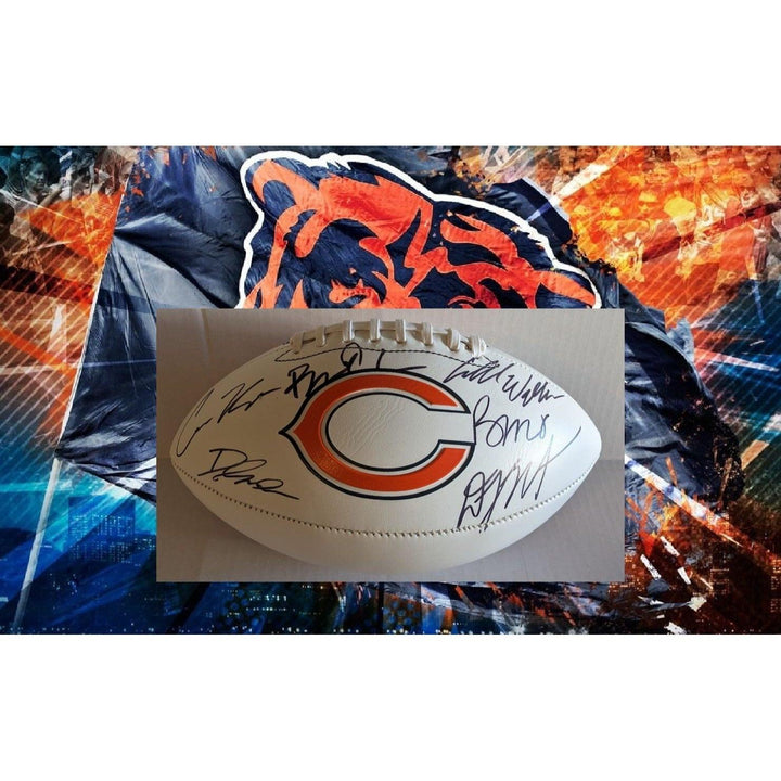A white football with team logo, autographs, and a vivid orange and blue bear-themed background.