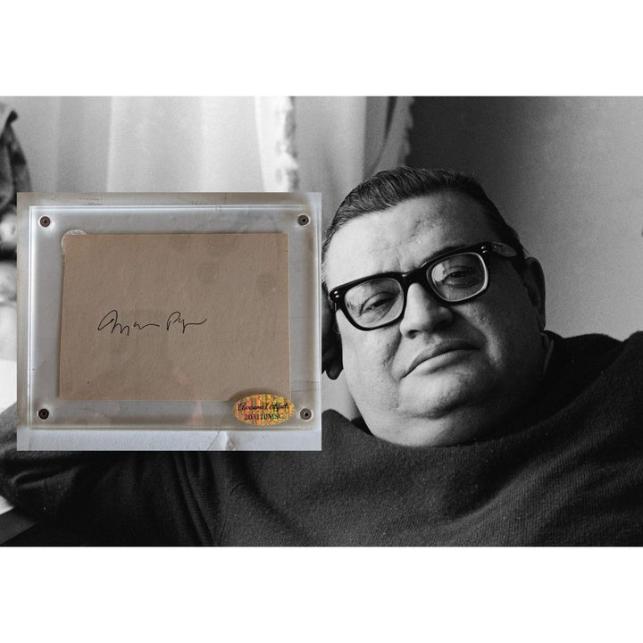 A black and white photo of a man with glasses and a signed card in a frame beside him.