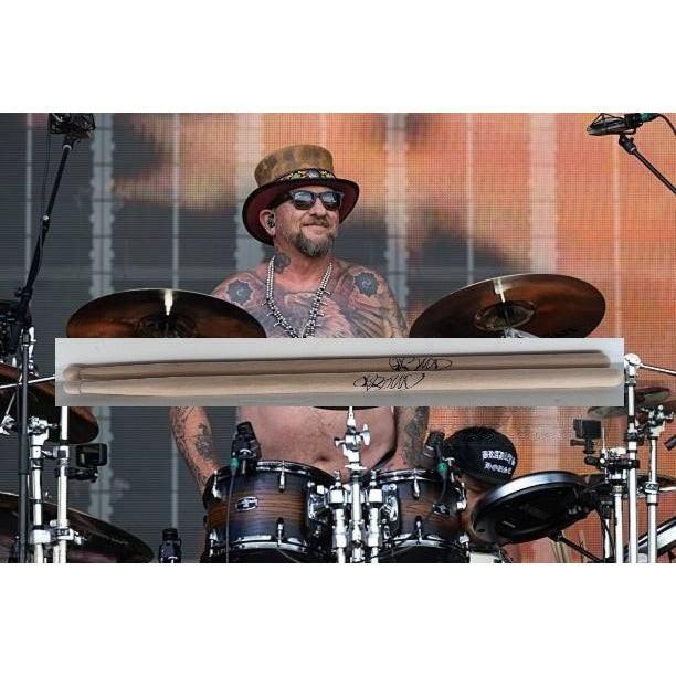 Tattooed drummer in a hat playing drums on stage with a colorful backdrop.