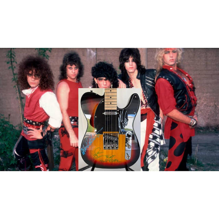 Band members in red and black outfits stand behind a sunburst electric guitar on a stand.