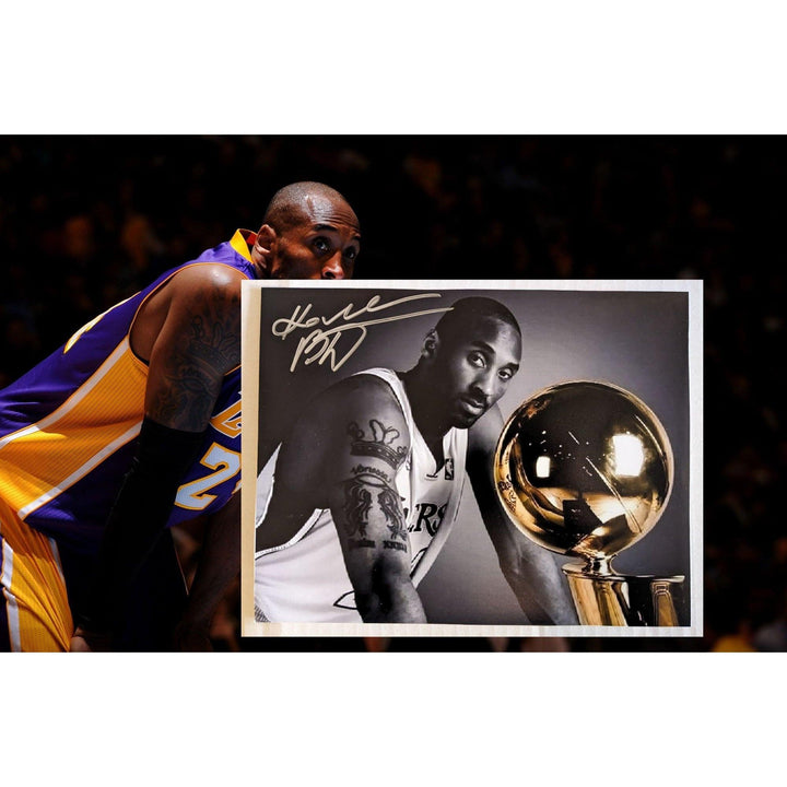 Basketball player in a purple and gold jersey with a signed black and white photo holding a trophy.