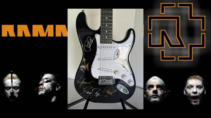 Black guitar with signatures centered on a dark background; orange text and geometric logos flanking.