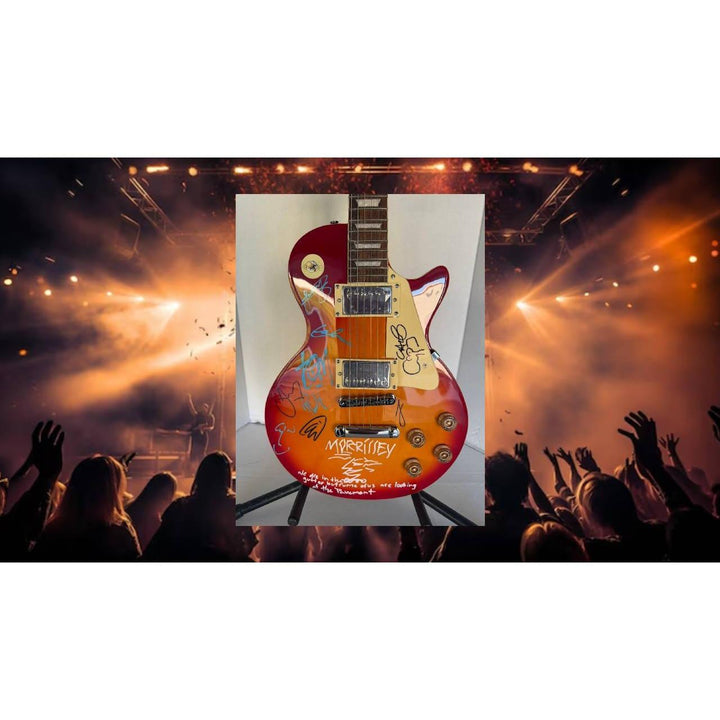 Electric guitar with colorful design on stage, with audience and bright lights in the background.