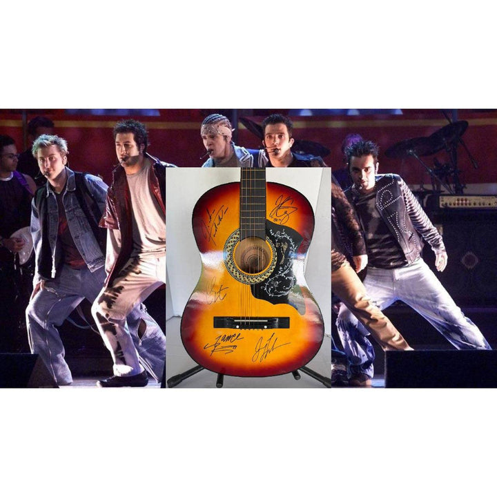 A group of performers dance on stage behind a sunburst acoustic guitar with signatures.
