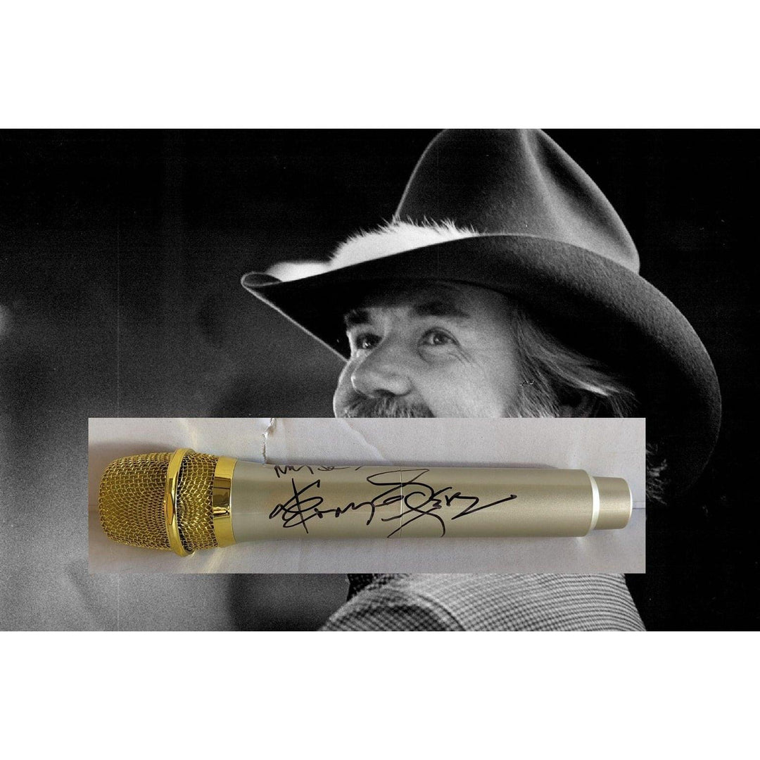 A black-and-white portrait of a smiling man in a cowboy hat with a signed gold microphone overlay.